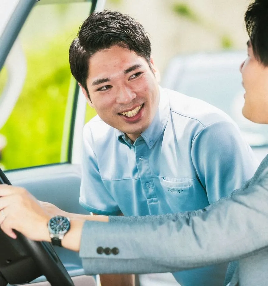 写真：男性社員が車に試乗しているお客様と笑顔で商談している様子