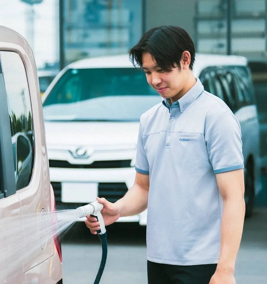 写真：男性スタッフが清掃用のシャワーを使い、車を掃除している様子